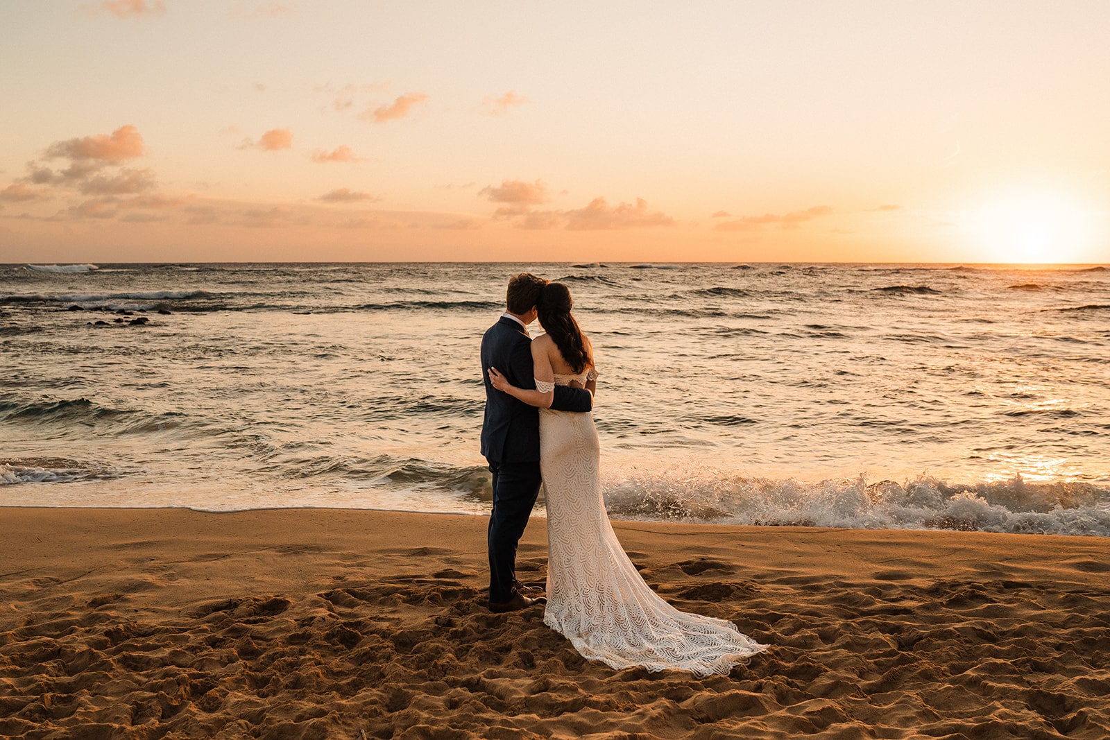 Bride and groom stand side by side watching the sun go down during their Kauai beach elopement in Hawaii. 