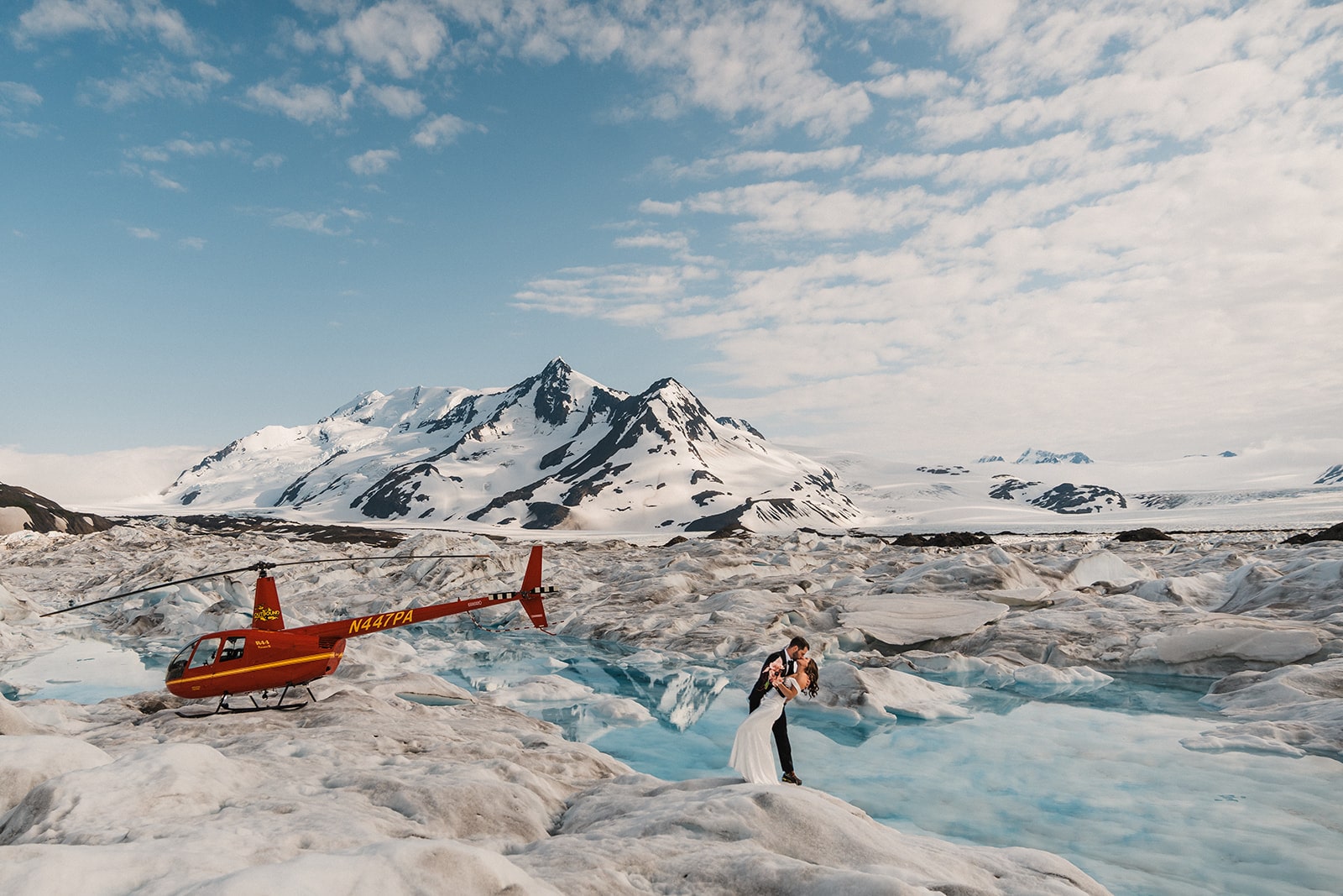 Groom dips bride back for a kiss on an Alaskan glacier during their helicopter tour.
