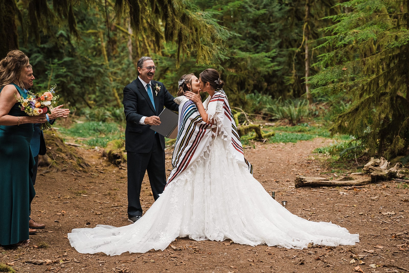 Two brides kiss at their elopement ceremony with a striped blanket wrapped around their shoulders.