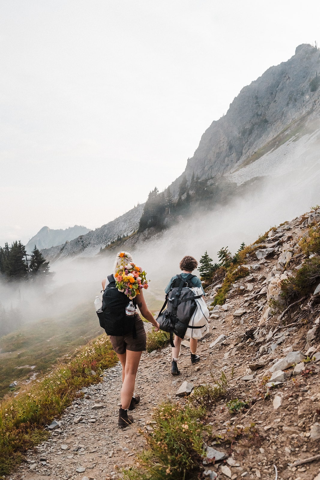 Man and woman hike up a foggy mountain trail with hiking backpacks. 
