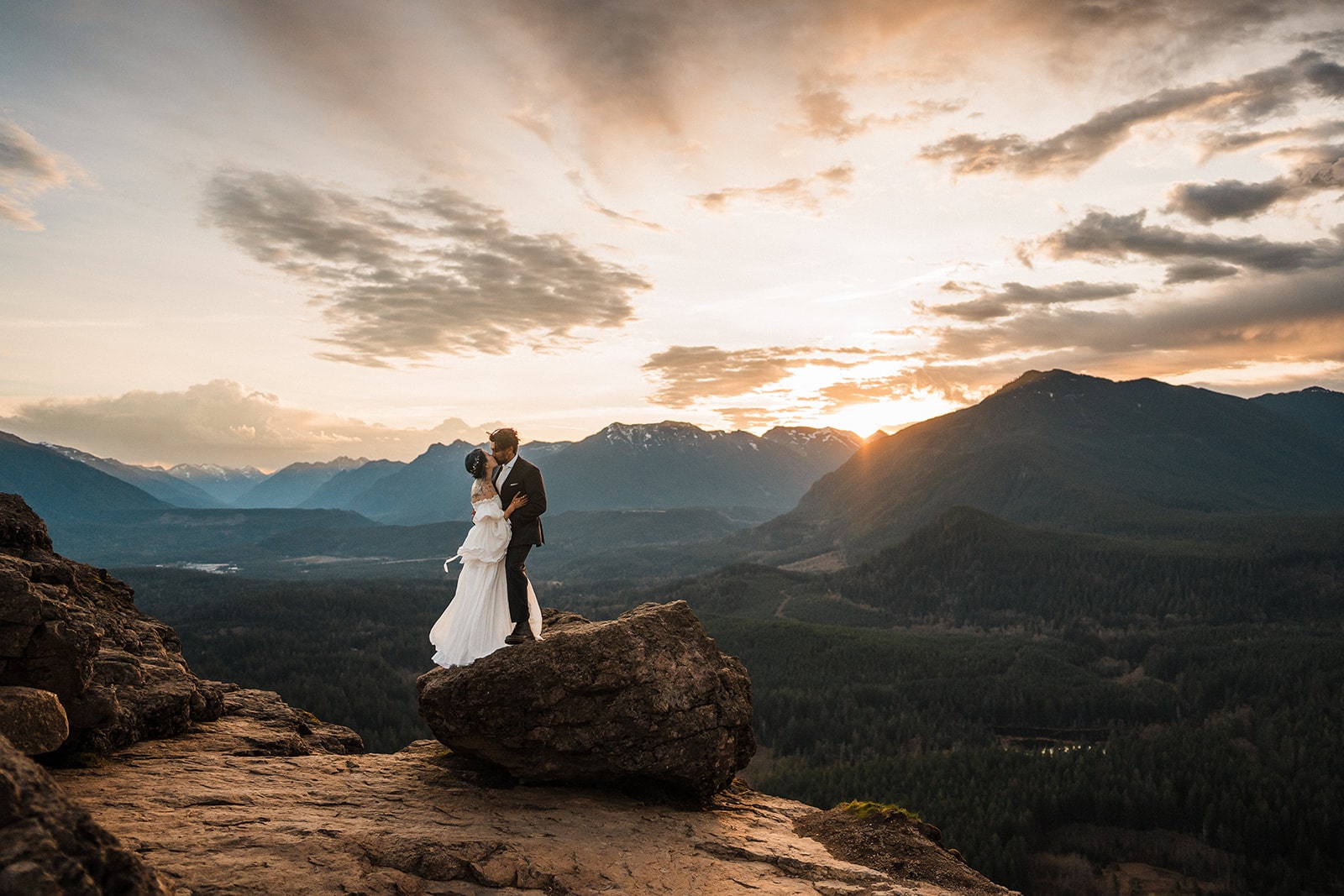 Bride and groom kiss on a mountaintop in Snoqualmie, Washington during sunrise.