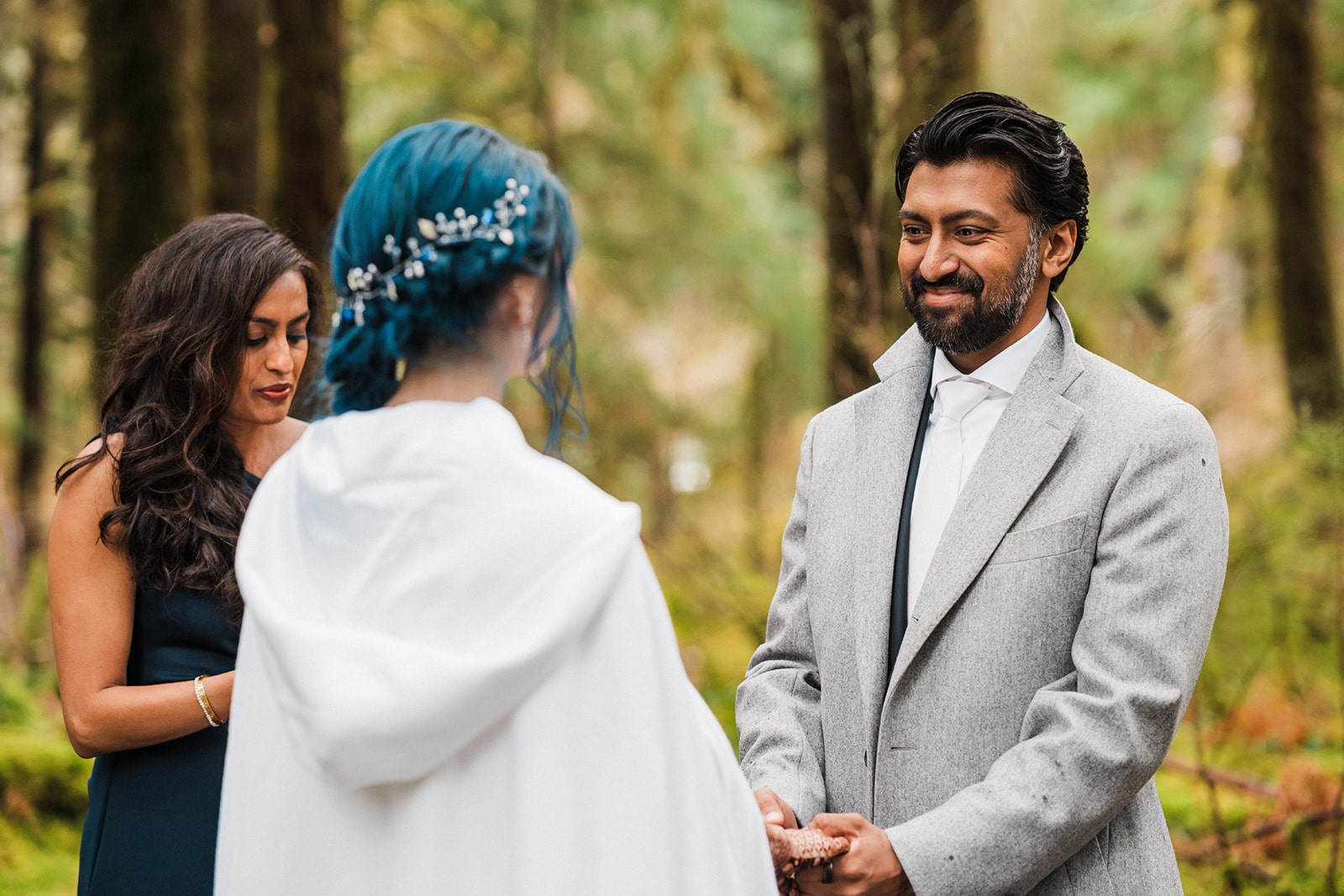 Groom smiles at bride during their forest elopement ceremony with family. 