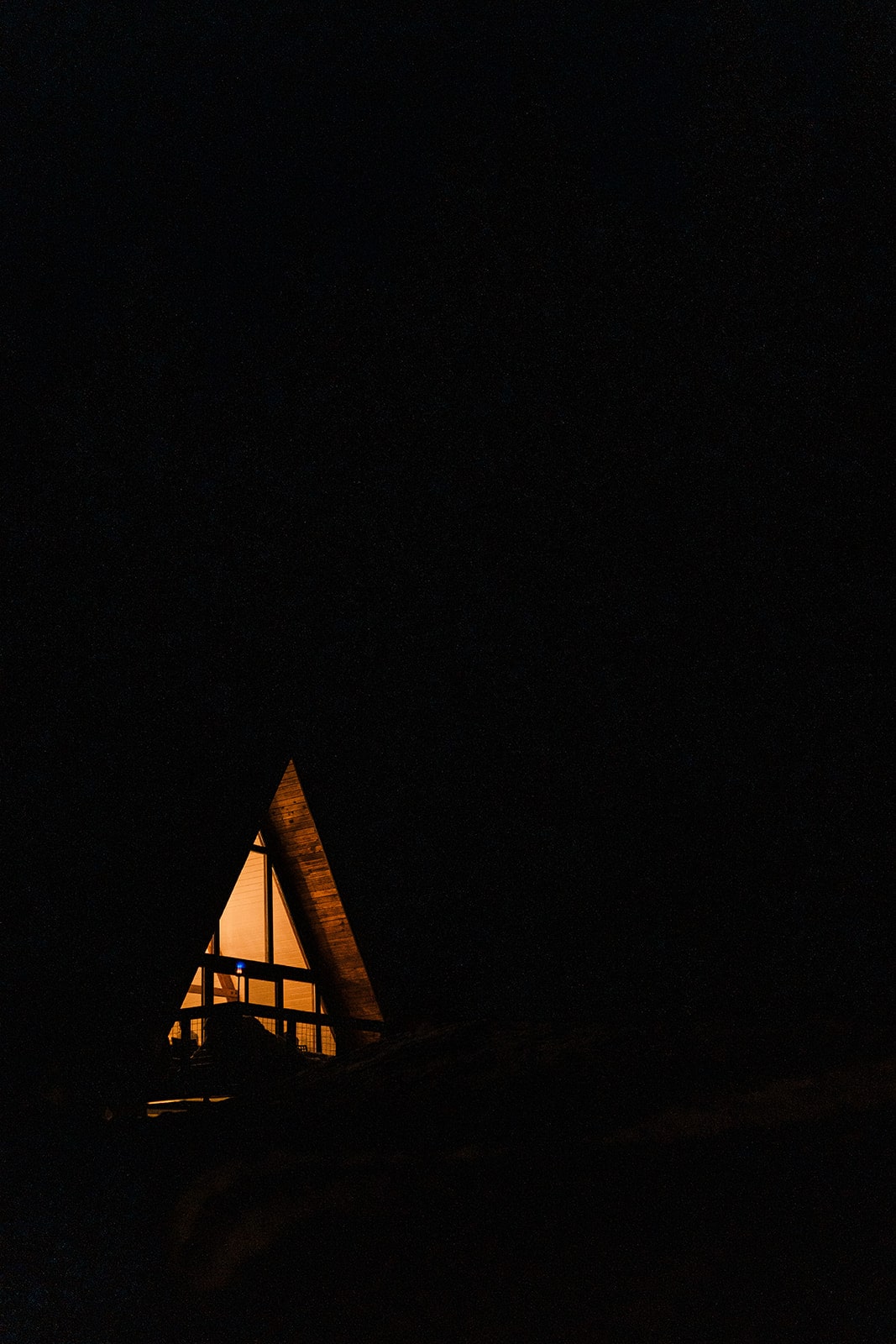 Lights from an A-frame cabin shine in the dark. 
