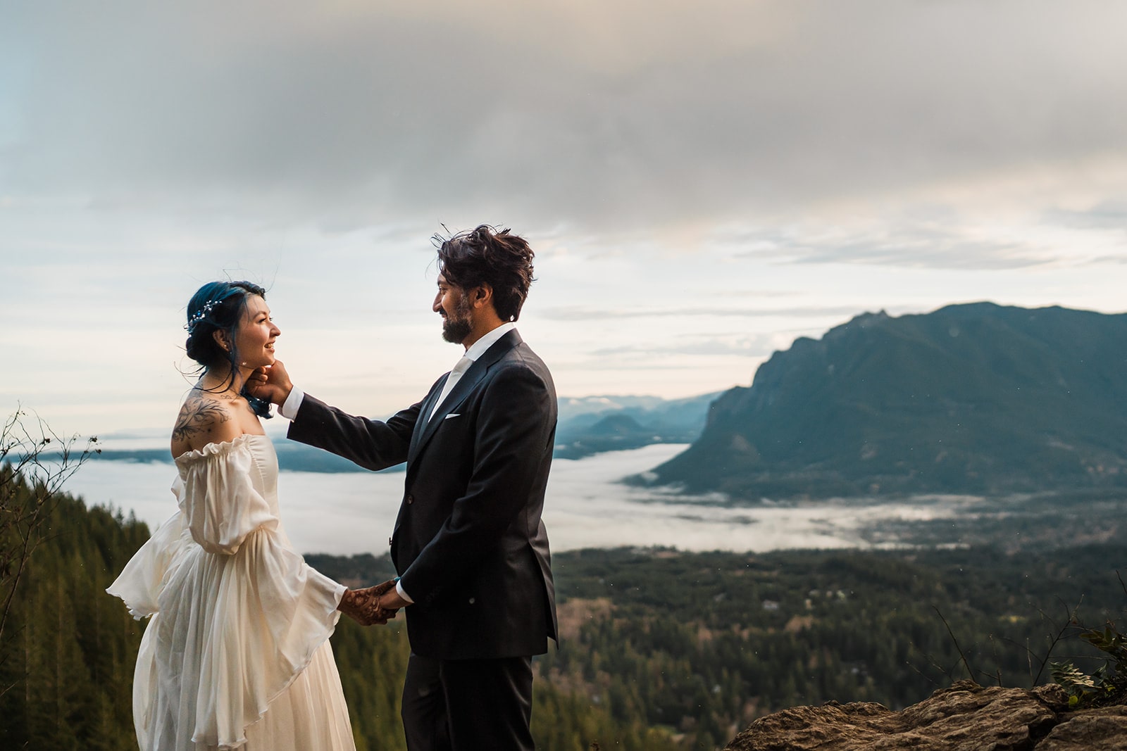 Bride and groom hold hands on a mountain trail as the clouds roll back during their sunrise elopement photos. 