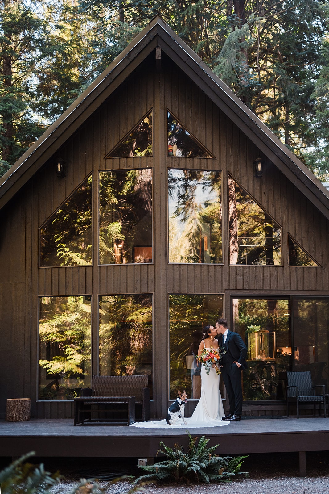 Bride and groom kiss in front of their A-frame cabin during their dog friendly elopement.
