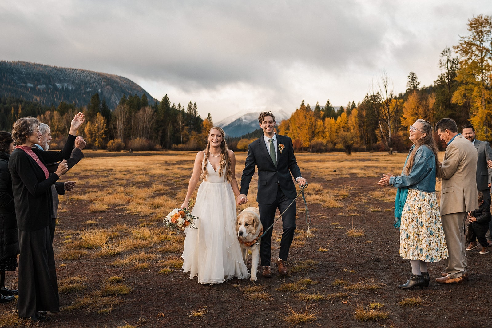 Guests cheer while bride and groom walk with their dog after their elopement ceremony.