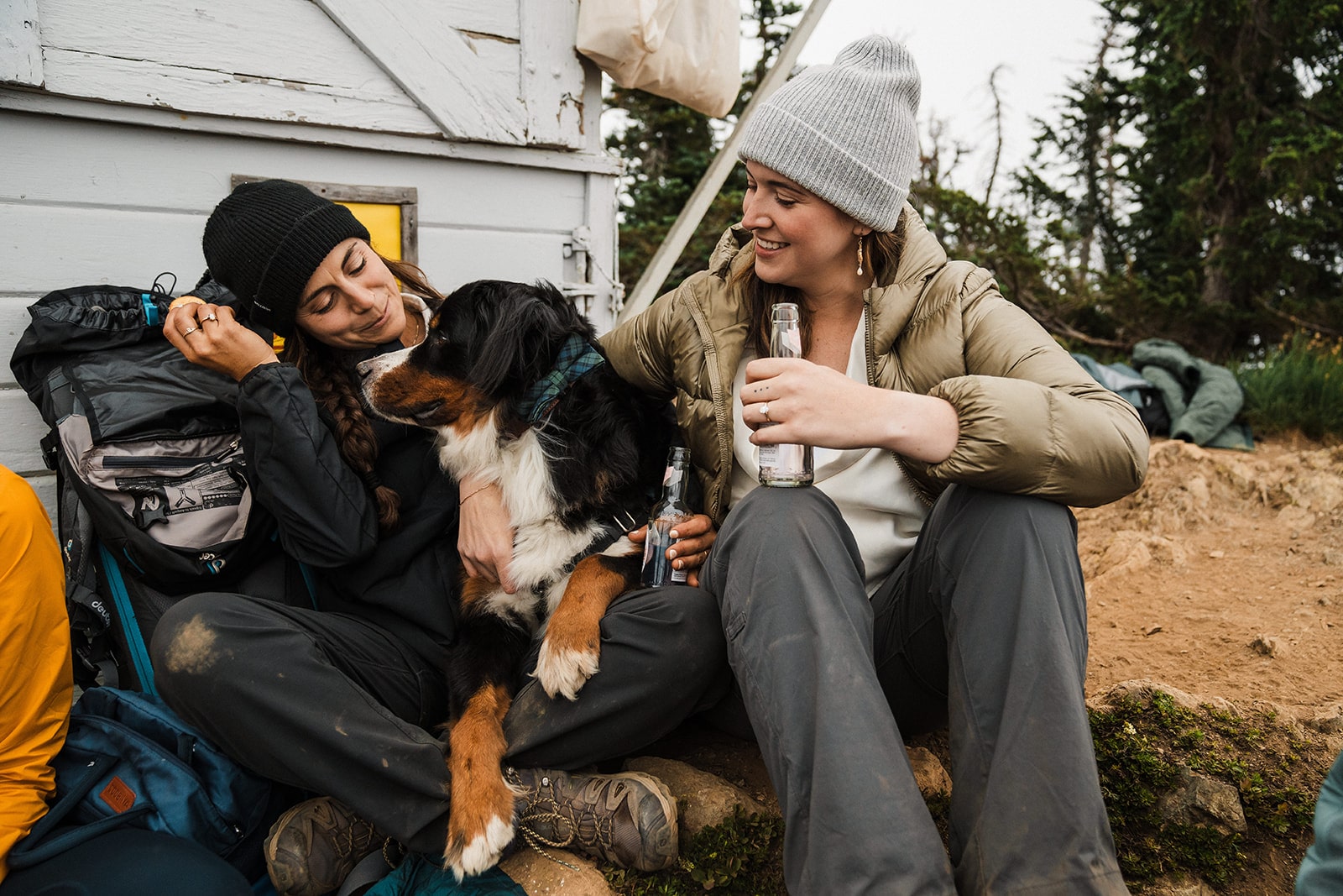 Two women sit with their dog at the top of a mountain trail during their adventure elopement in Washington.