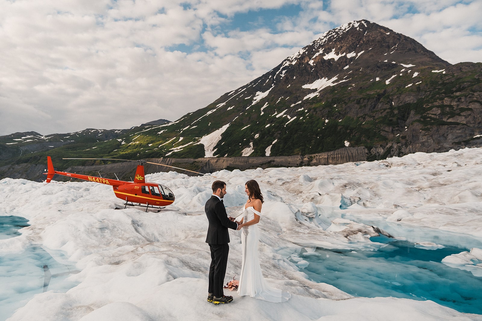 Bride and groom hold hands on a glacier during their helicopter elopement in Alaska. 