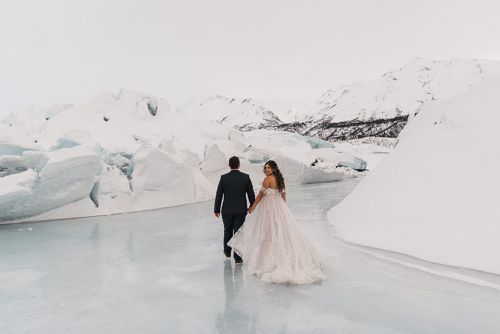 Bride and groom hold hands while walking on an ice covered lake during their elopement in Alaska. 
