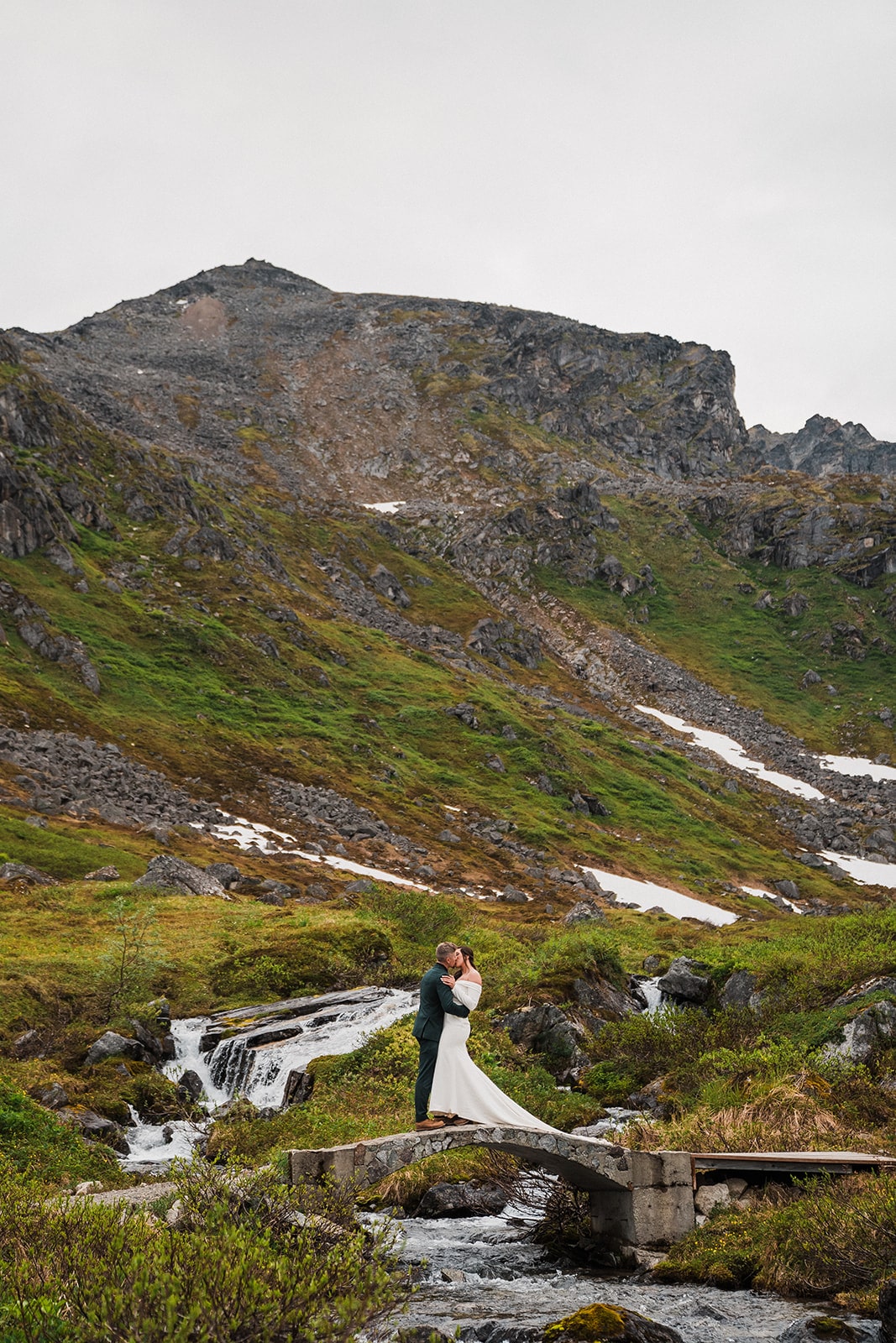 Bride and groom kiss on a bridge over a creek during their elopemetn in Alaska. 