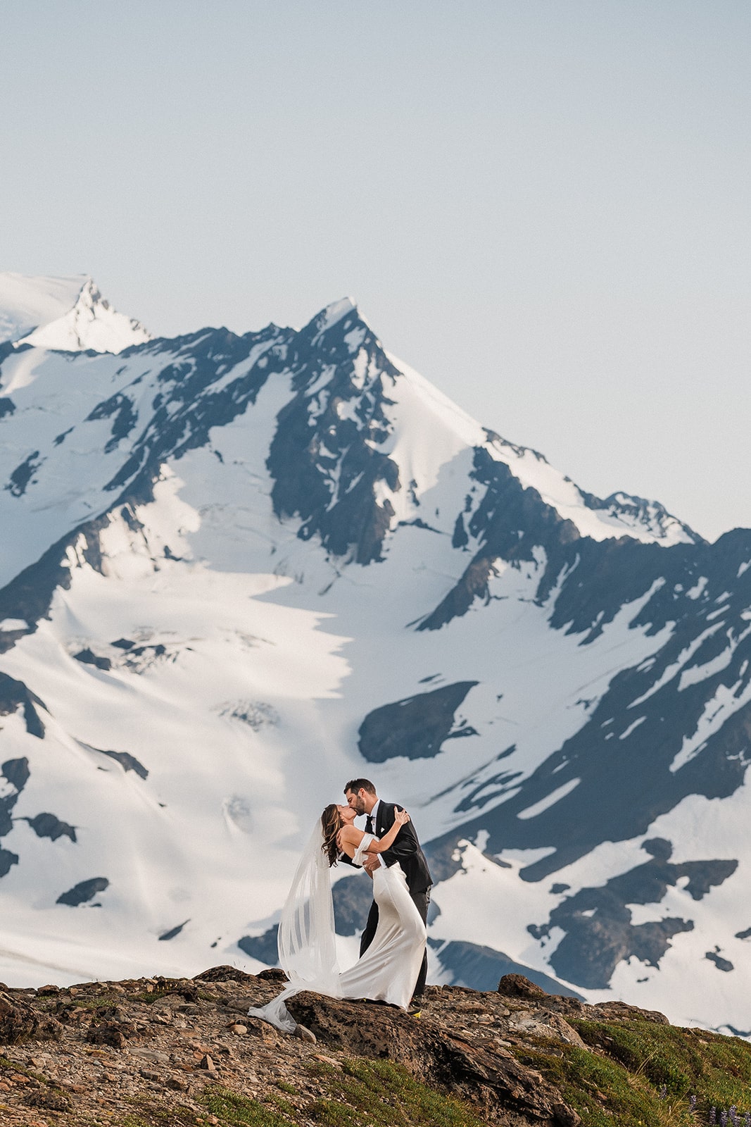 Groom dips bride for a kiss in front of a snow mountain at their Alaska elopement. 