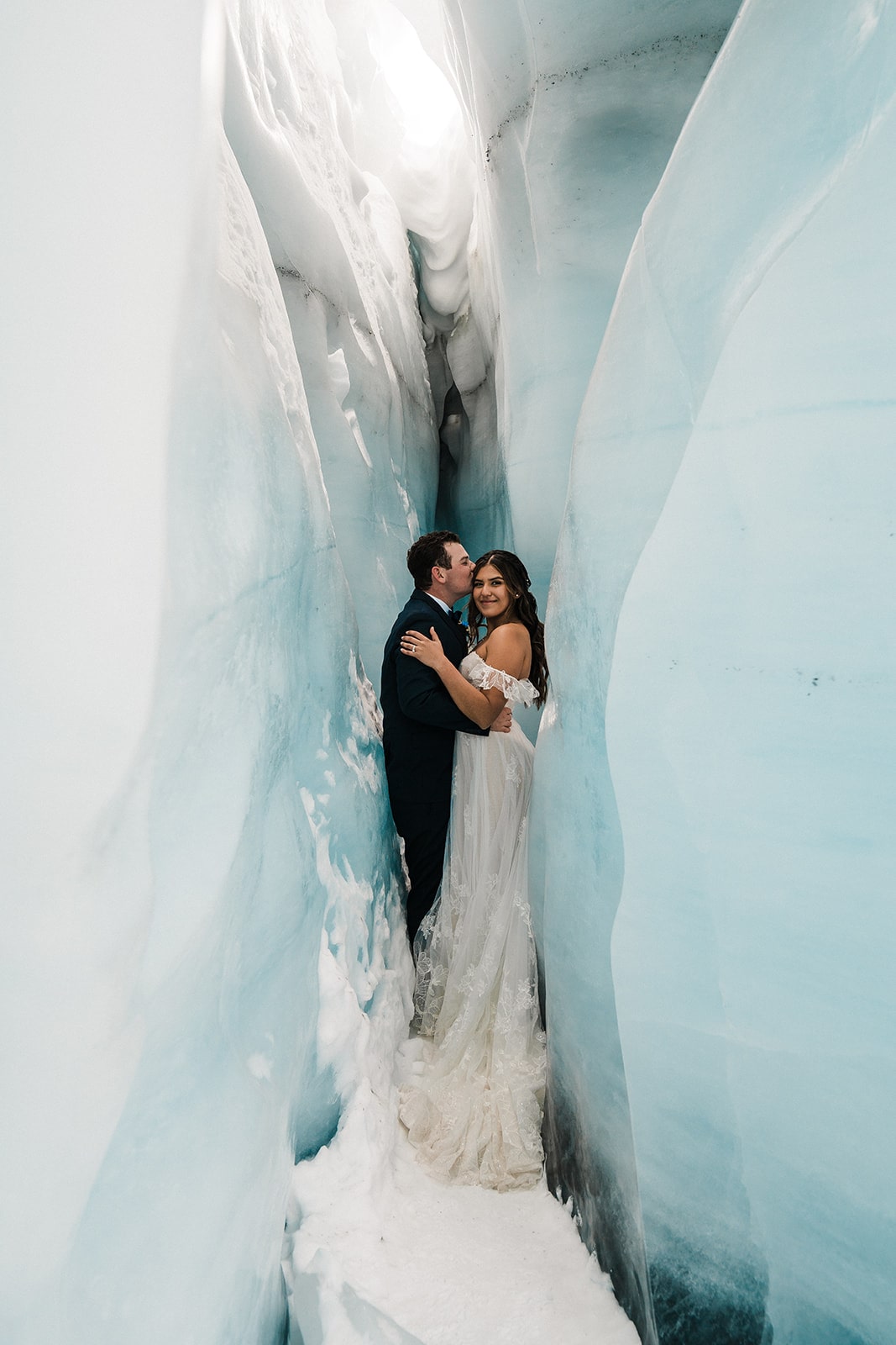 Groom kisses bride on the head while standing in an ice cave in Alaska. 