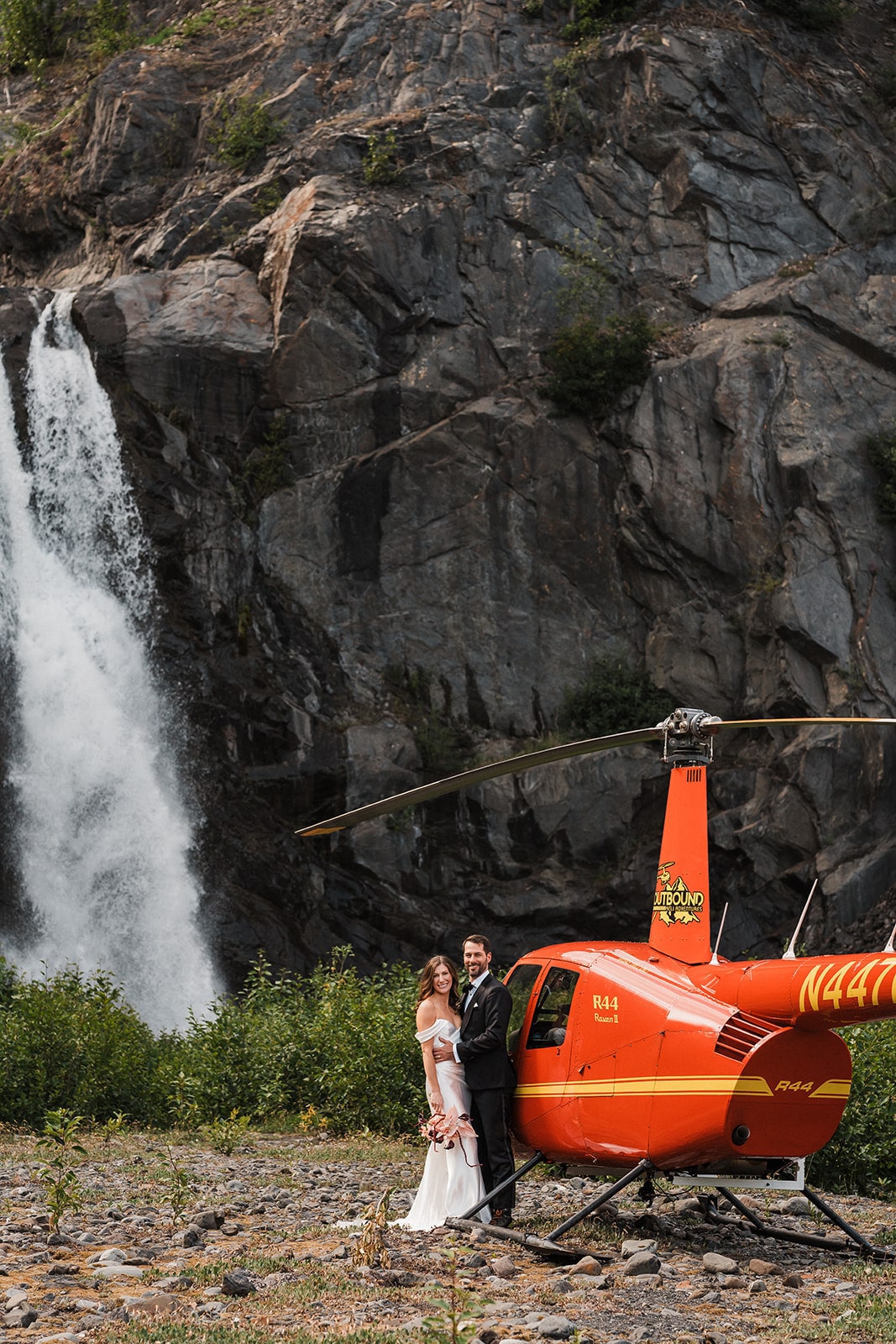 Bride and groom stand next to a red helicopter during their elopement in Alaska with Outbound Heli.