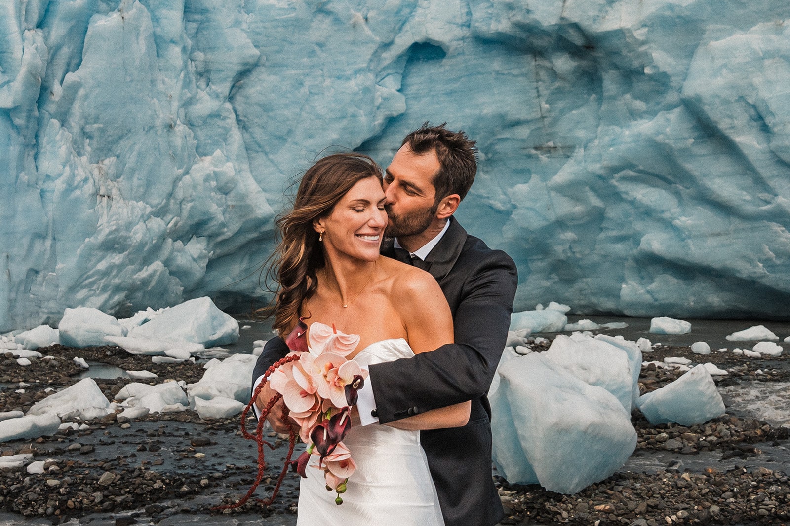 Groom hugs bride from behind during their elopement adventure with multiple locations in Alaska.