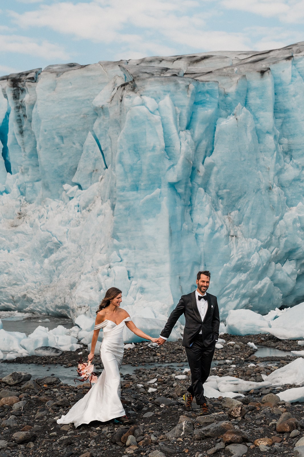 Bride and groom hold hands as they walk around a glacier in Palmer, Alaska on their elopement day.