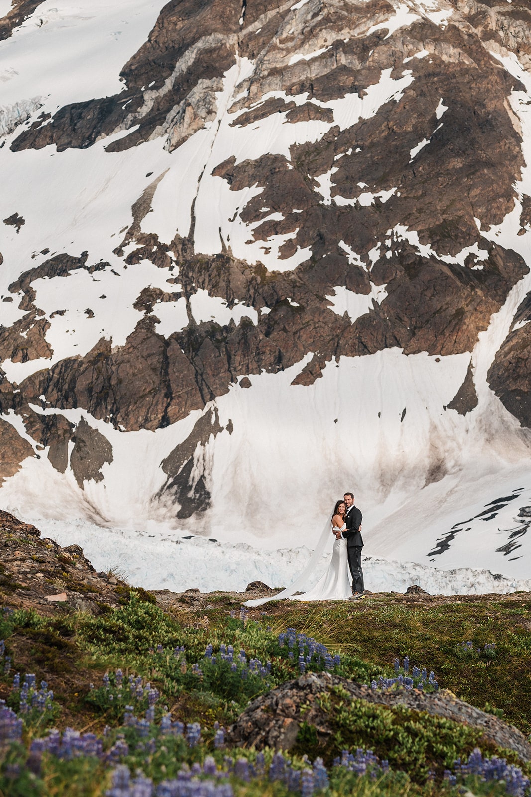 Bride and groom hug on a mountain trail during their adventure wedding in Alaska.