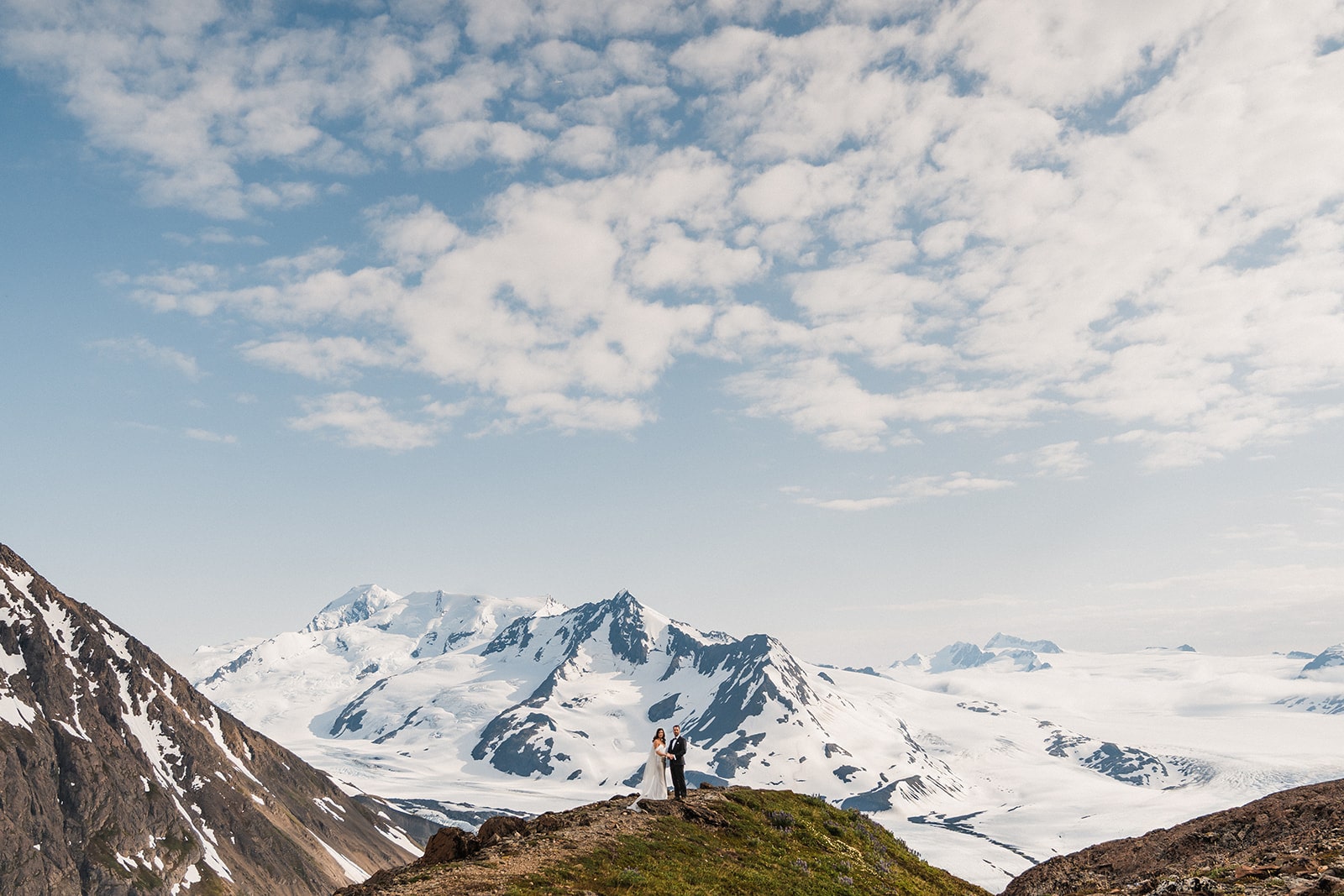 Bride and groom hold hands on a mountain trail during their multi-adventure elopement in Alaska.