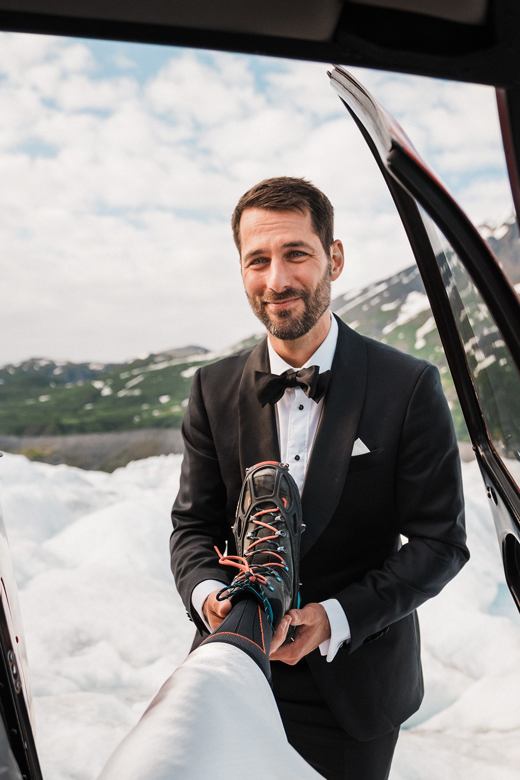 Groom helps bride put on her ice shoes during their snowy glacier elopement in Alaska.