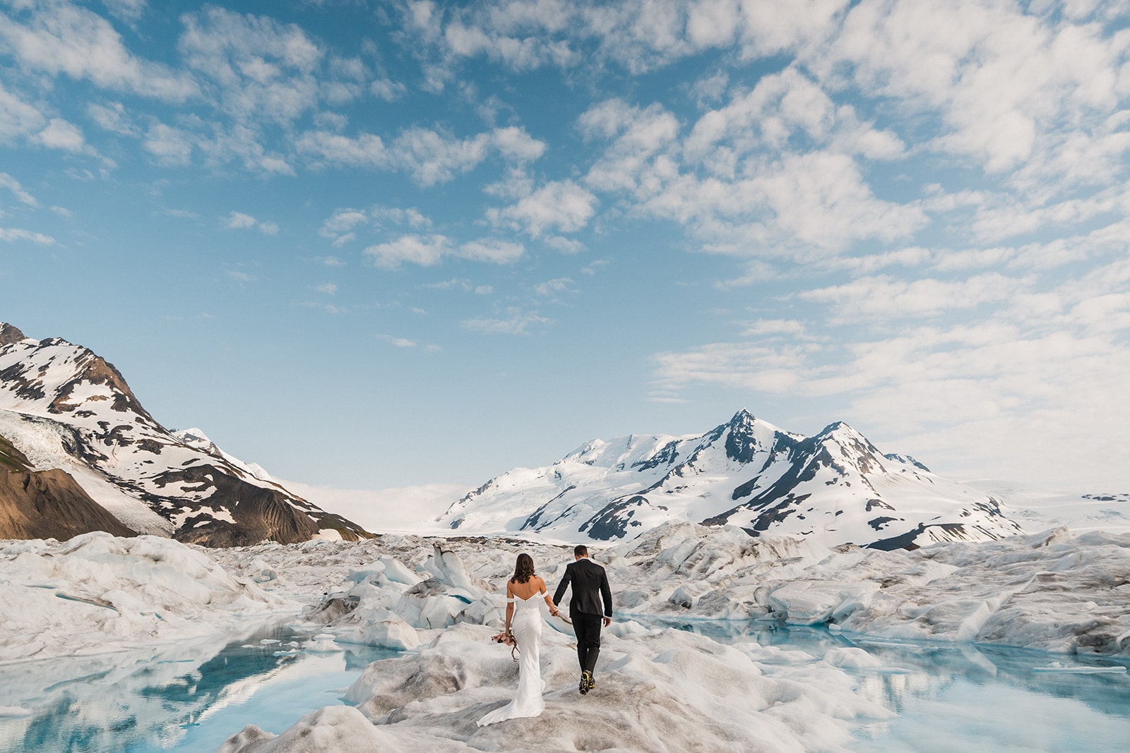 Bride and groom hold hands during their snowy glacier elopement in Palmer, Alaska.