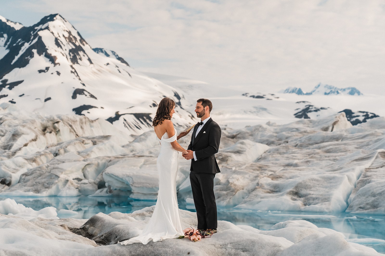Bride reads vows to groom during their elopement ceremony on a snowy Alaskan glacier.