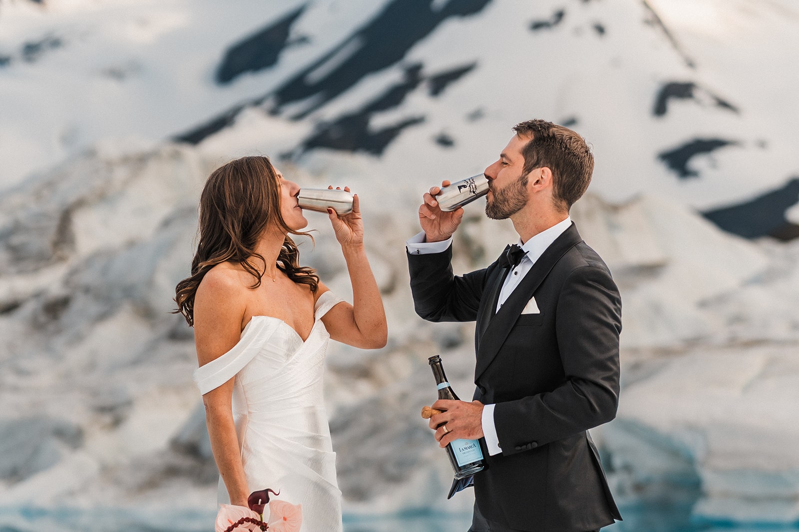 Bride and groom drink champagne from silver glasses during their Alaska glacier elopement.