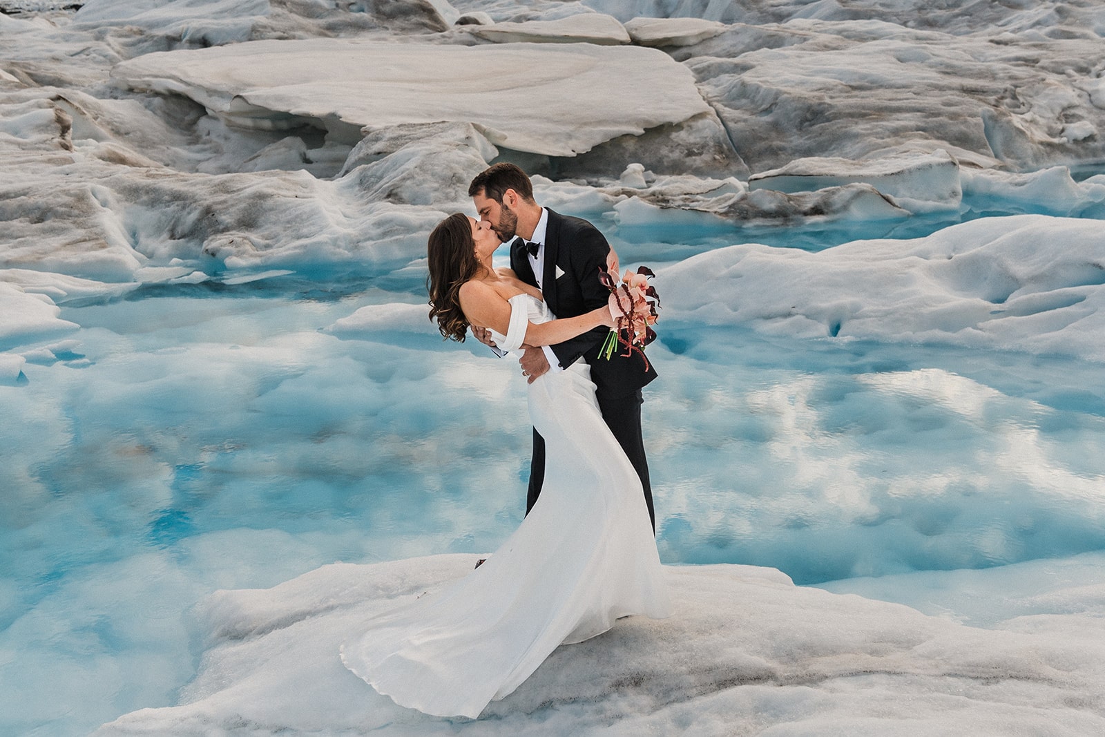 Bride and groom kiss on a snowy Alaskan glacier during their elopement with Outbound Heli Adventures.