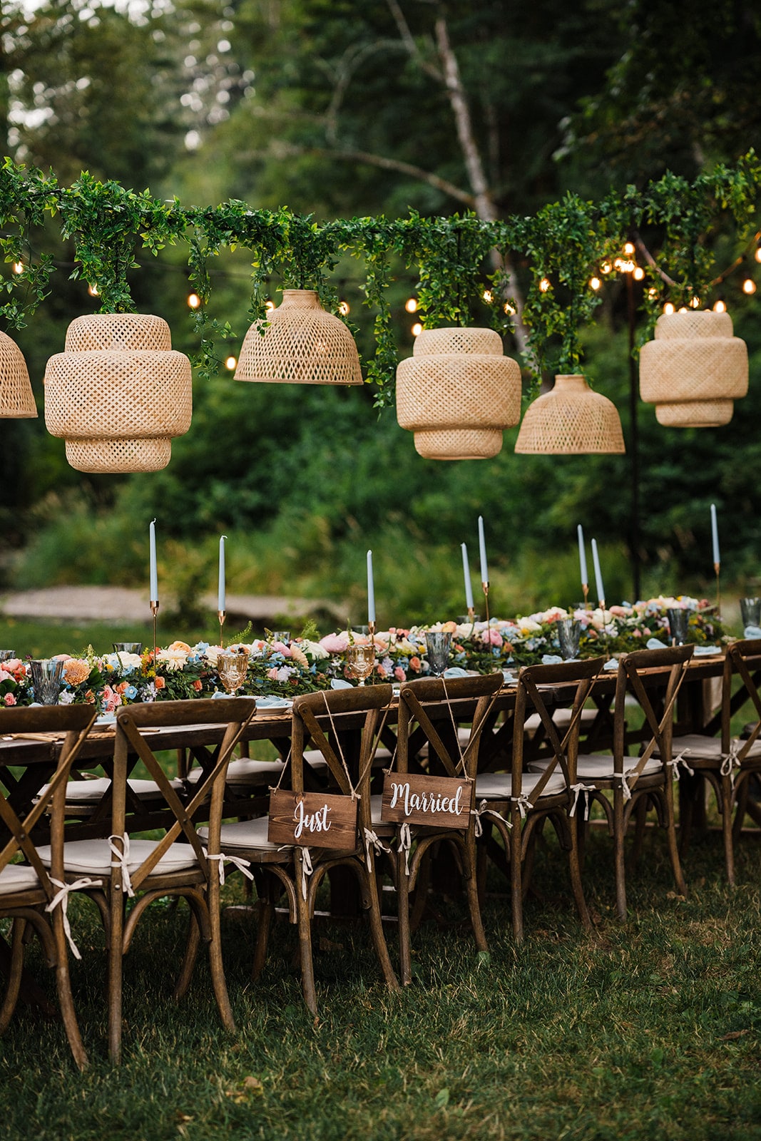 Backyard wedding reception table under wicker lights and greenery. 