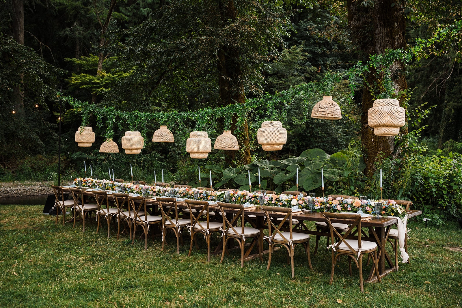 Long wood table with wicker lights hanging above at an outdoor wedding reception in Washington. 