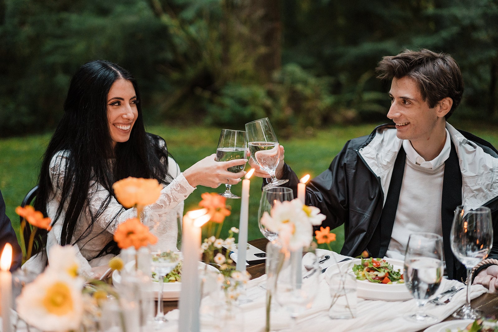 Bride and groom toast glasses during their intimate wedding reception dinner in the forest. 