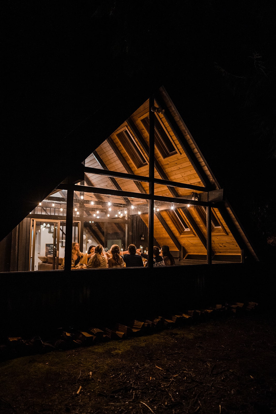 Guests sit around a dinner table under string lights during their cabin micro wedding reception in Washington. 