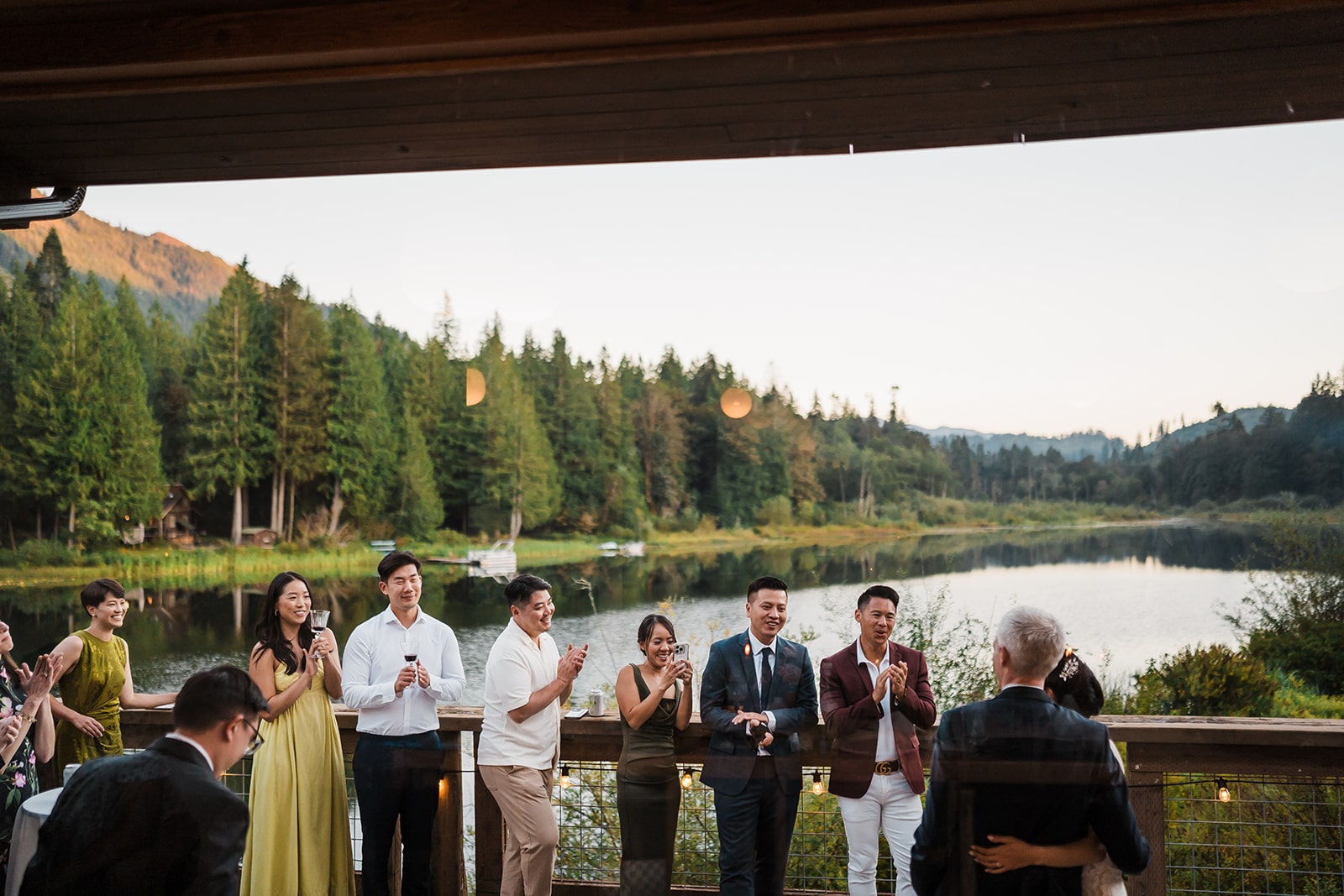 Guests mingle on a deck overlooking a lake at a state park micro wedding reception in Washington. 