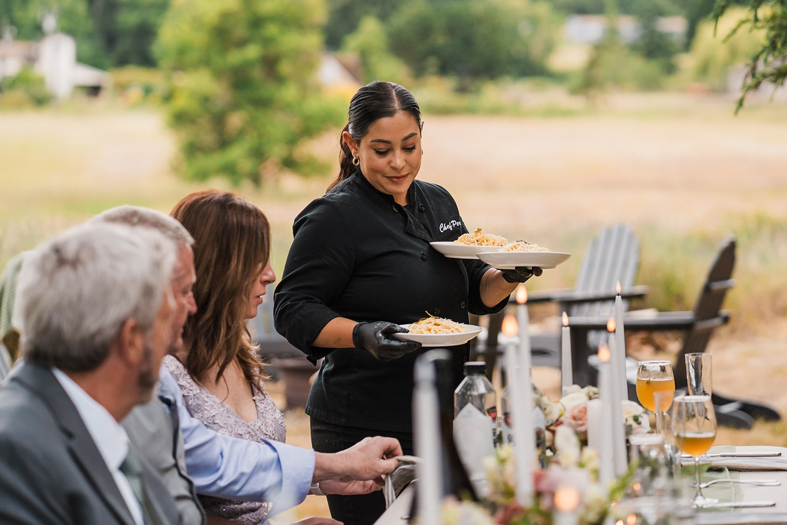 Private chef serves plates of food to wedding guests at an outdoor dinner reception. 