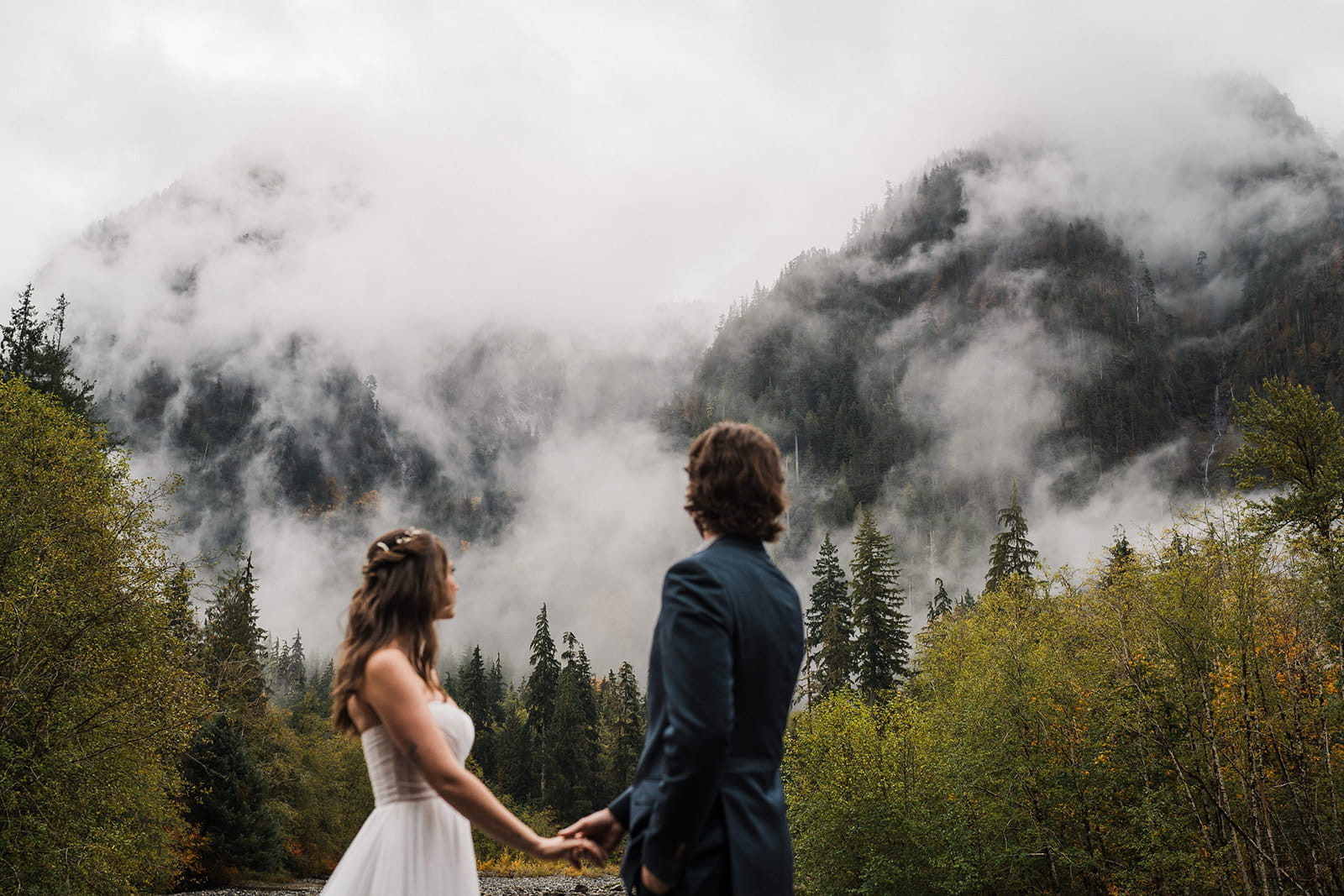 Bride and groom hold hands and look up at the cloudy mountains during their Washington rainy wedding. 