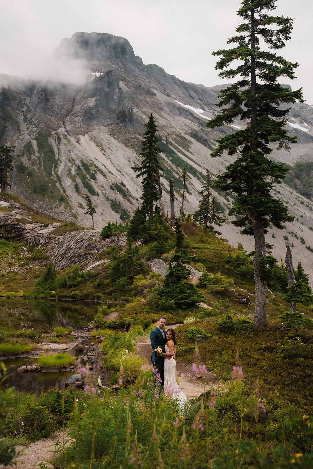 Bride and groom stand on a mountain trail during their cloudy elopement day in Washington. 