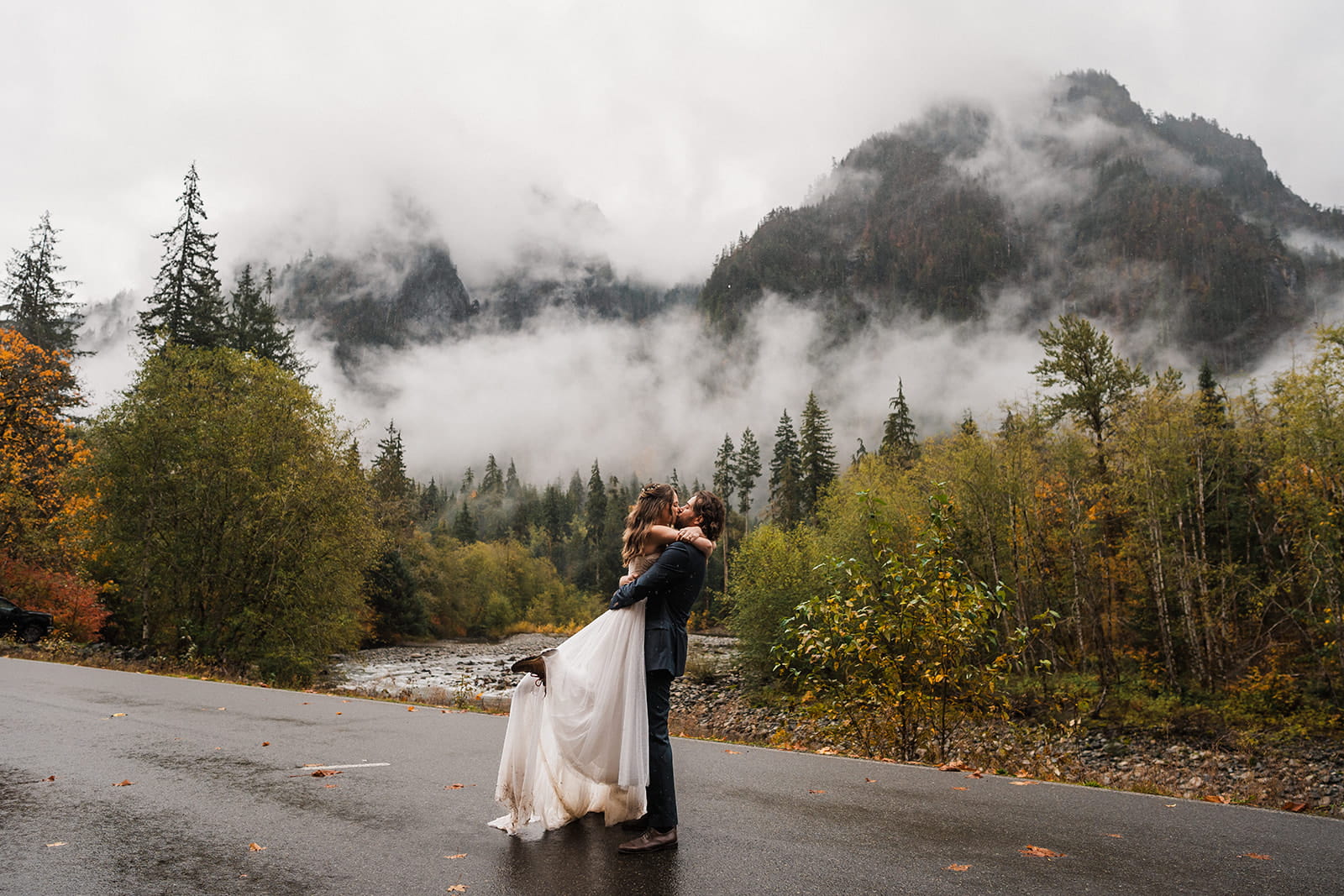 Bride and groom kiss on a mountain road during their cloudy, rainy wedding day in Washington.