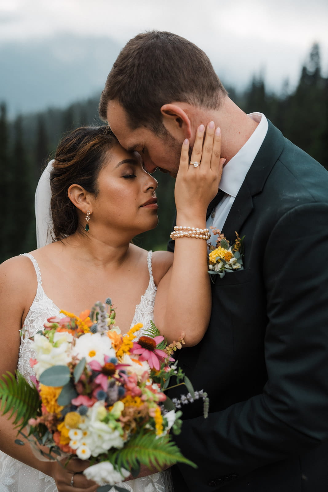 Bride reaches up to touch groom's face during their rainy wedding portraits in the Washington mountains. 