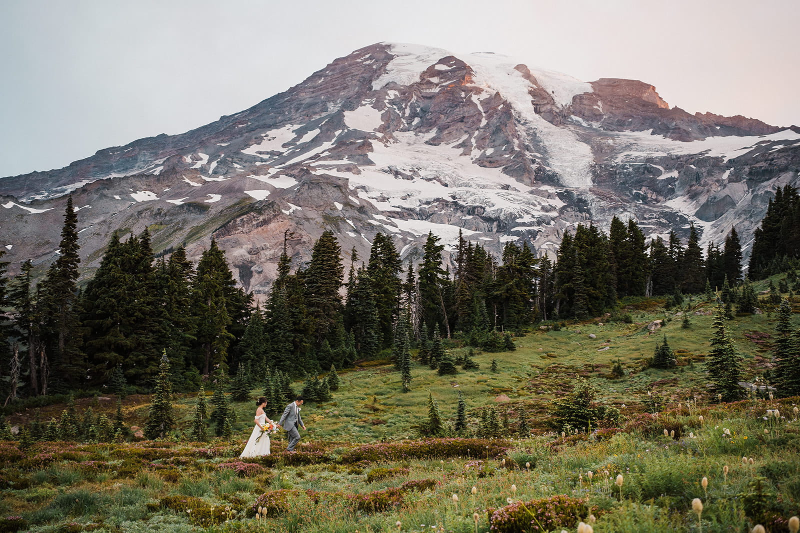 Bride and groom hold hands while hiking a wildflower trail in Mt Rainier National Park. 