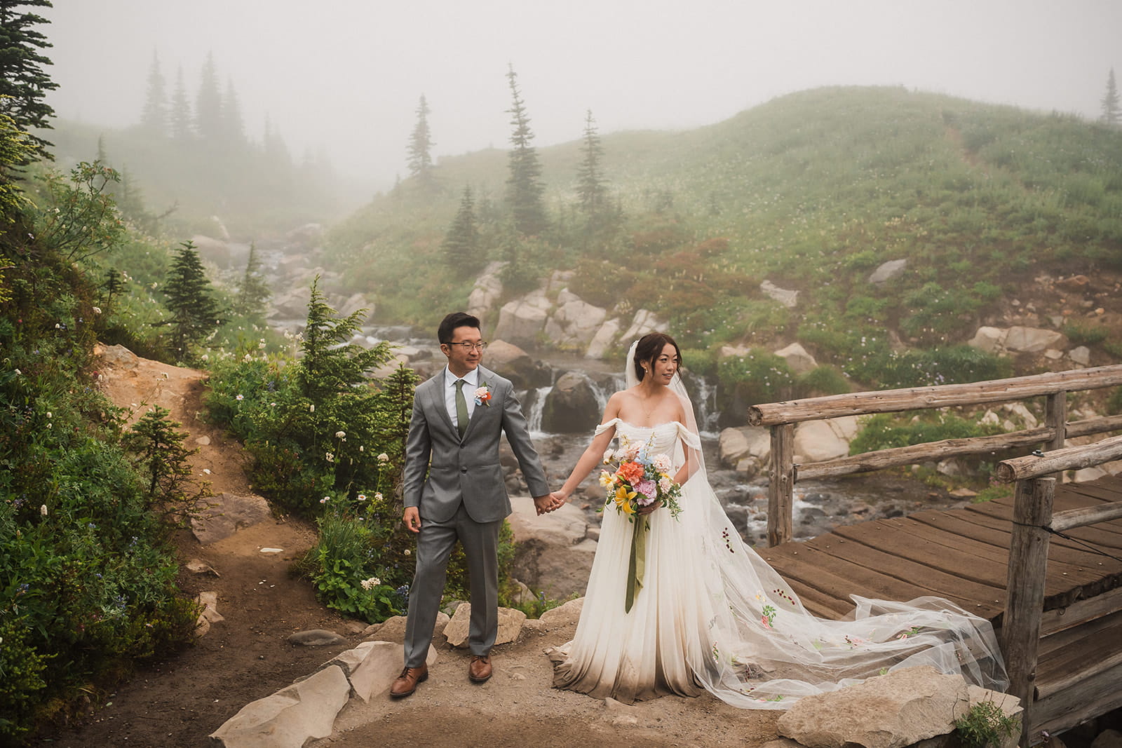 Bride and groom hold hands next to a stream during their sunrise elopement at Mt Rainier National Park. 