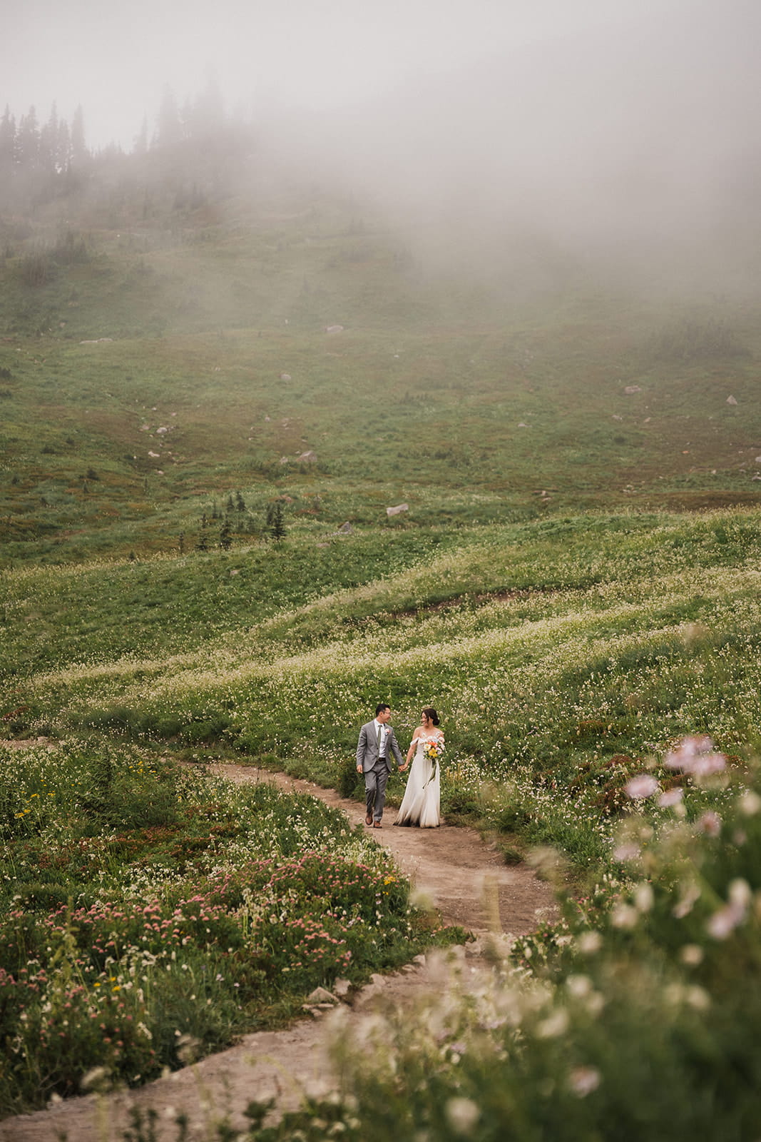 Bride and groom hold hands while hiking through a wildflower meadow trail in Washington. 
