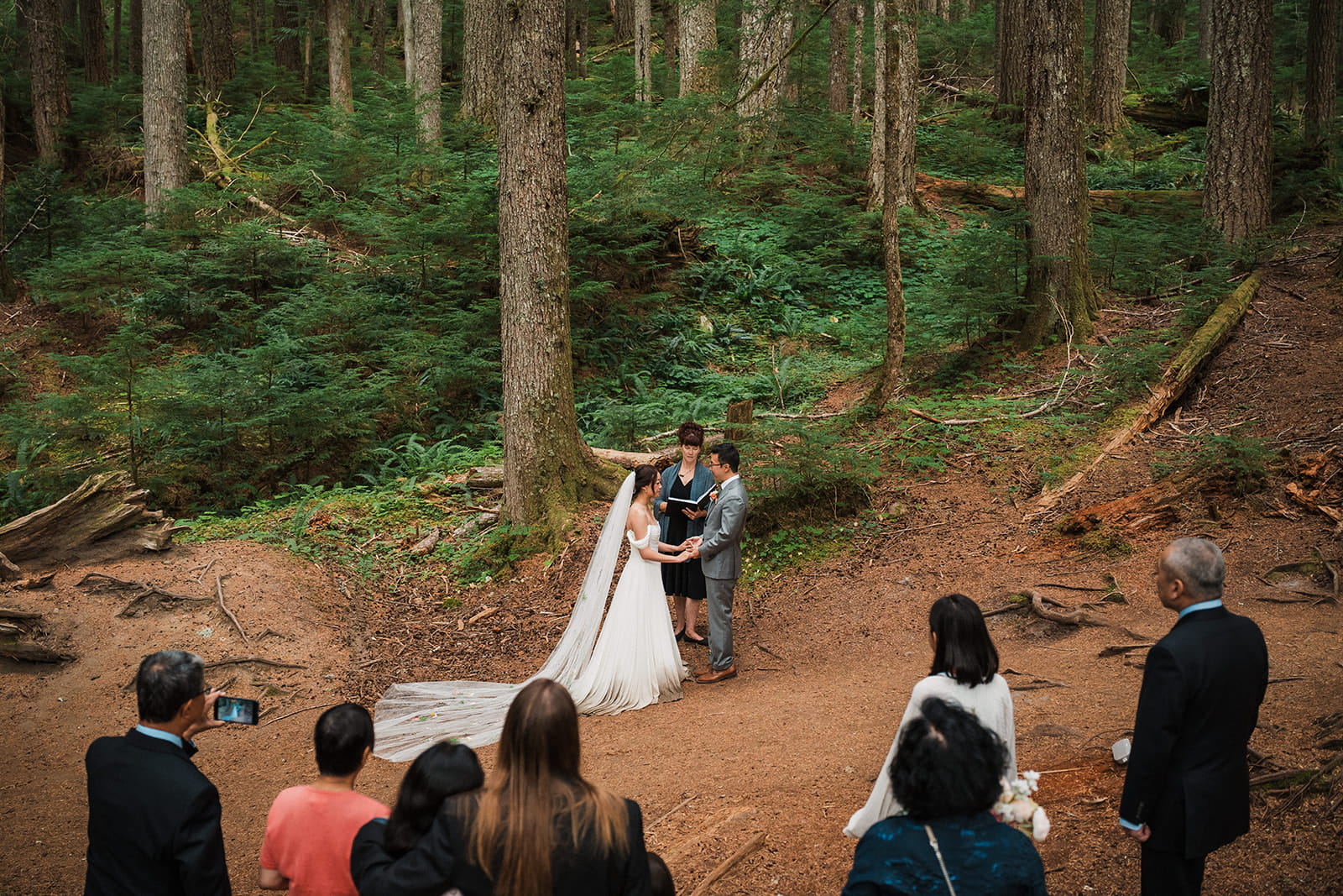 Bride and groom hold hands during their Washington forest wedding ceremony. 