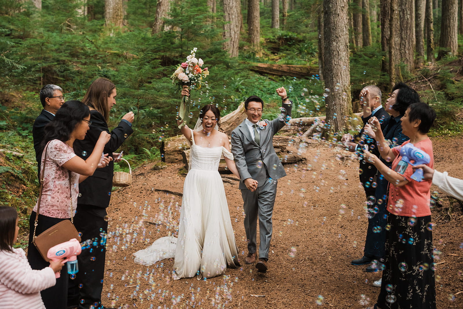 Bride and groom cheer while guests blow bubbles after their forest wedding ceremony in Washington State. 