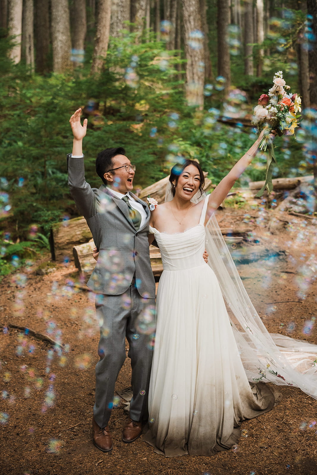 Bride and groom cheer surrounded by bubbles after their Mt Rainier forest wedding ceremony.