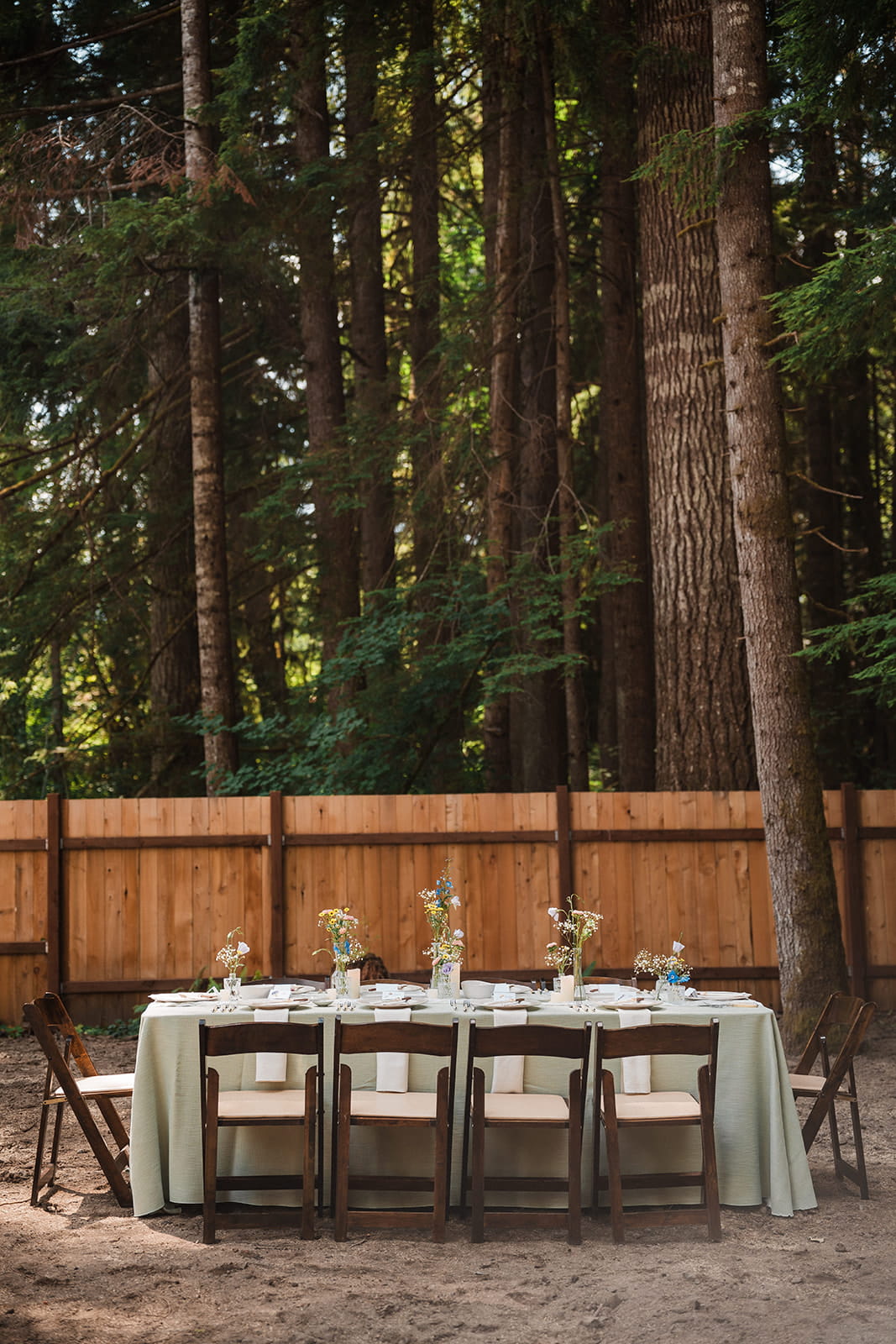 Forest wedding reception table with a sage green covering and wildflowers lining the center. 