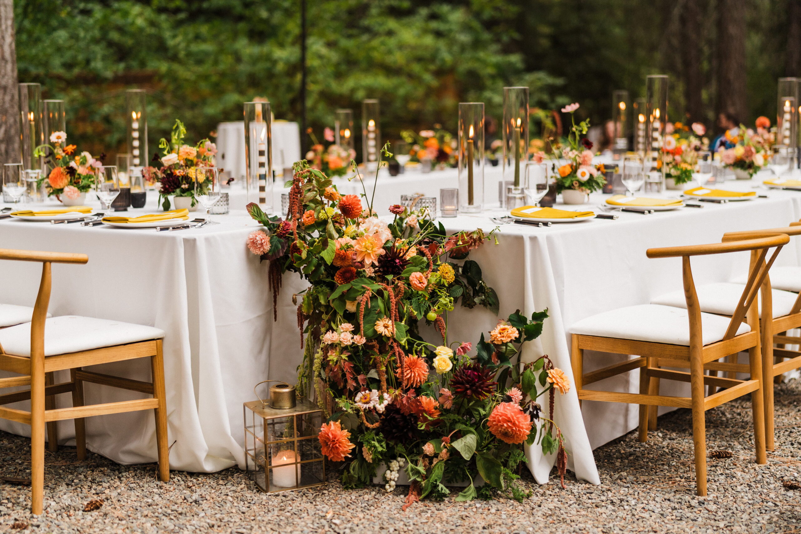 Floral arrangements cascade down white tables at an outdoor micro wedding reception dinner. 