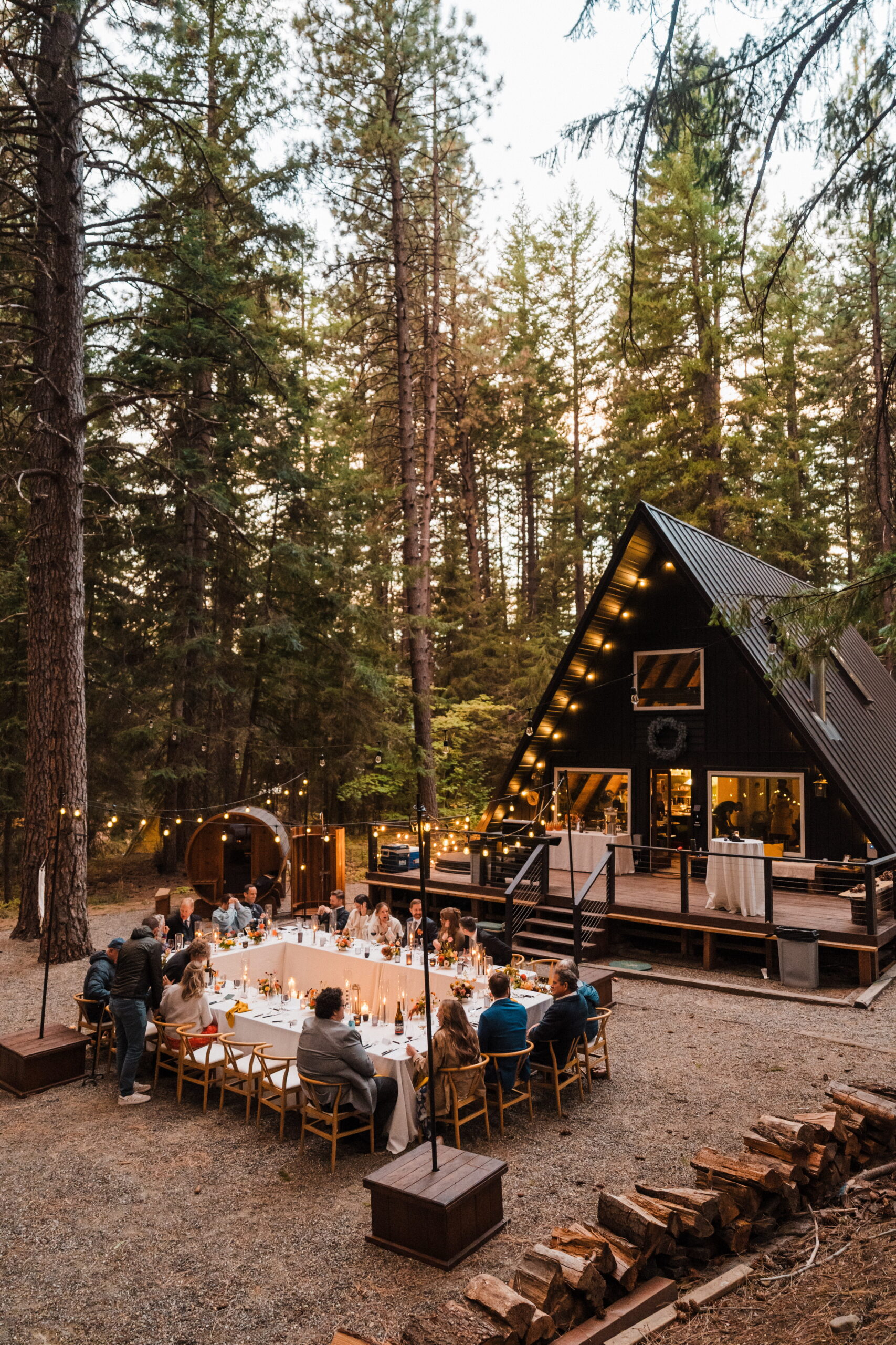 Guests mingle around reception dinner tables under string lights in front of an A-frame cabin in Snoqualmie. 