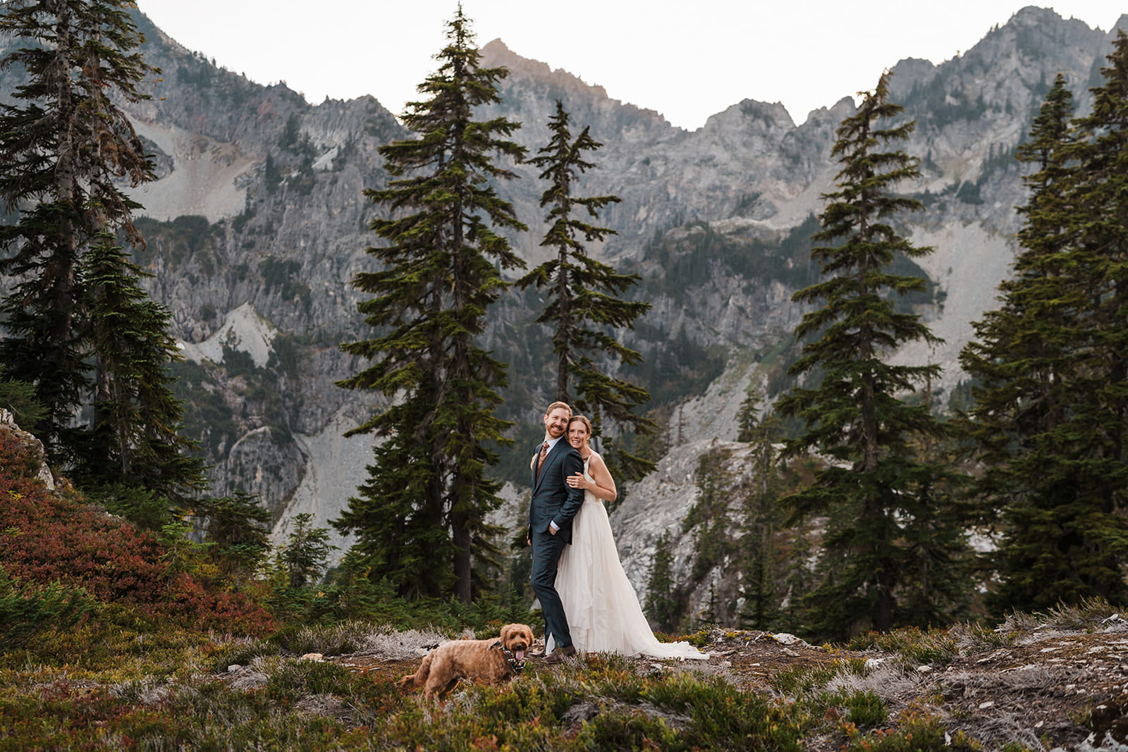 Newlyweds stand on a mountain trail with their pup during their backpacking elopement. 