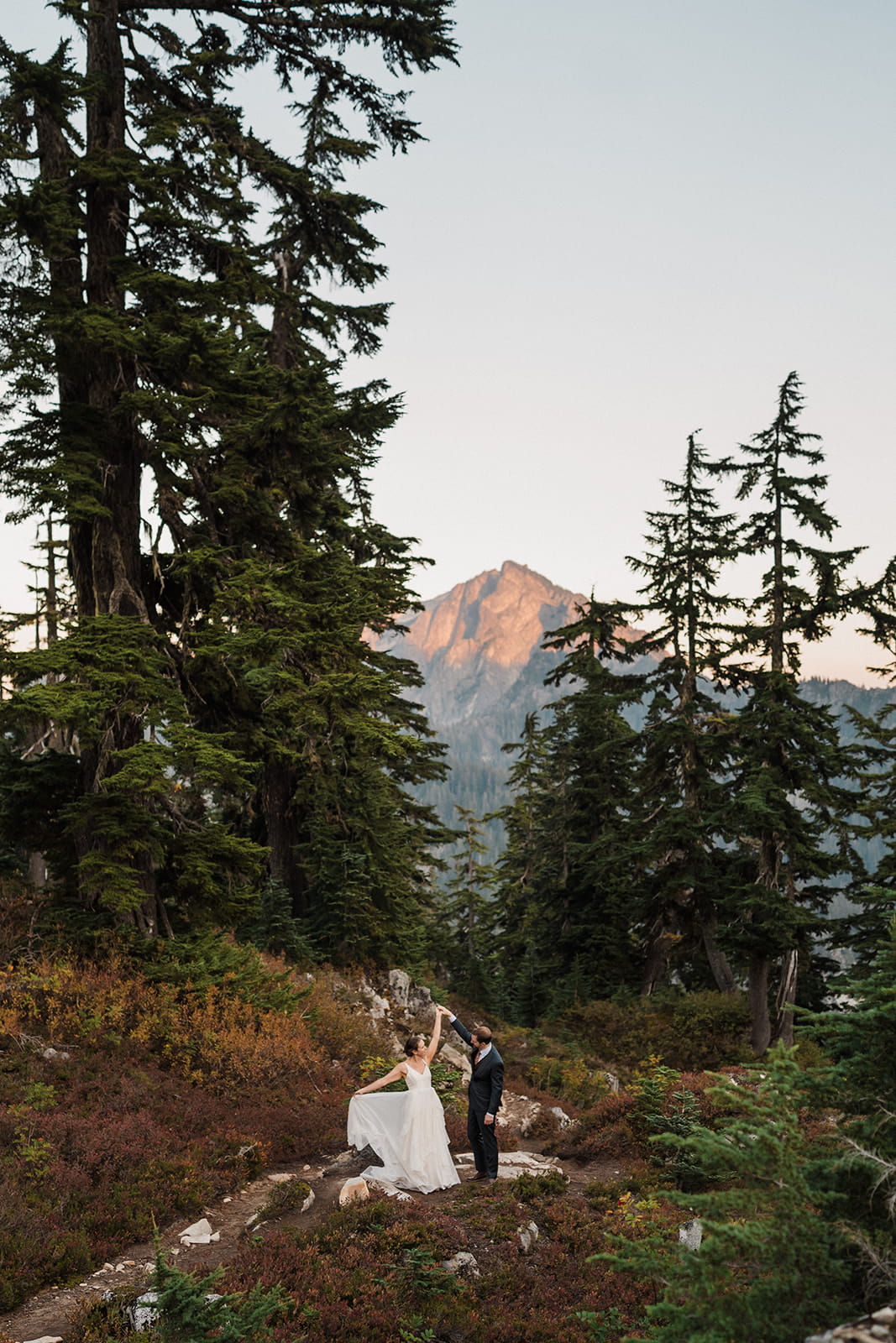Newlyweds dance on a mountain trail during their overnight backpacking elopement. 
