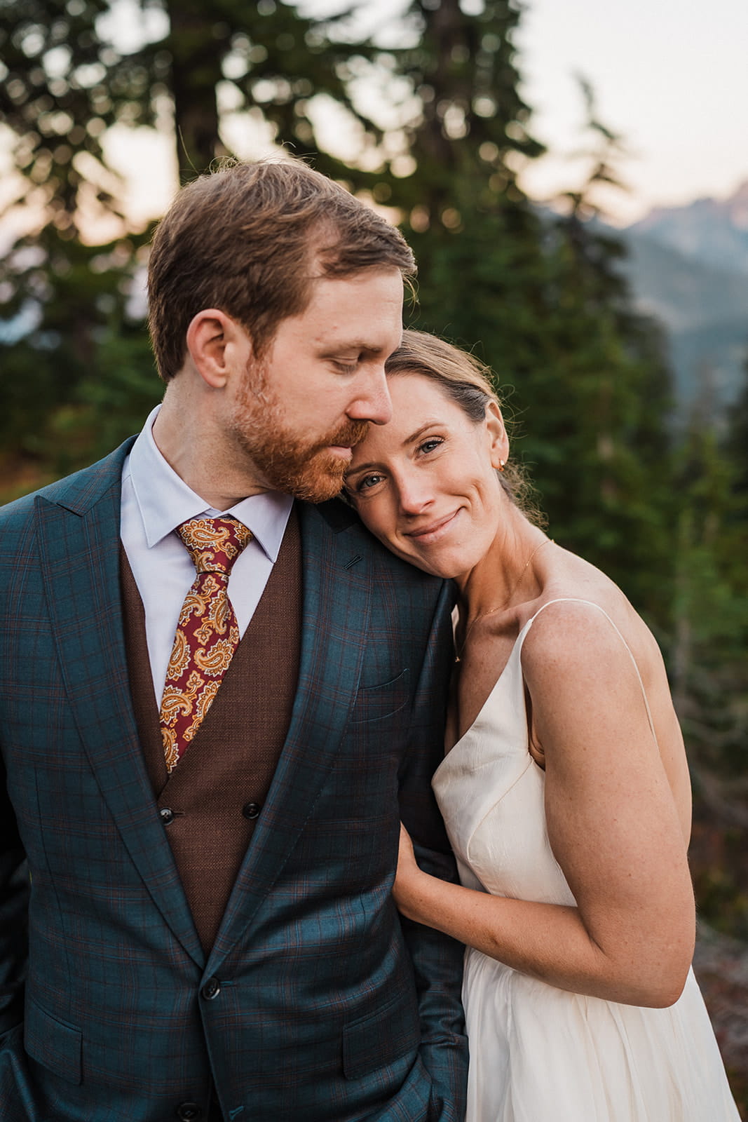 Bride rests her head on groom's shoulder during their hiking elopement portraits in the mountains.