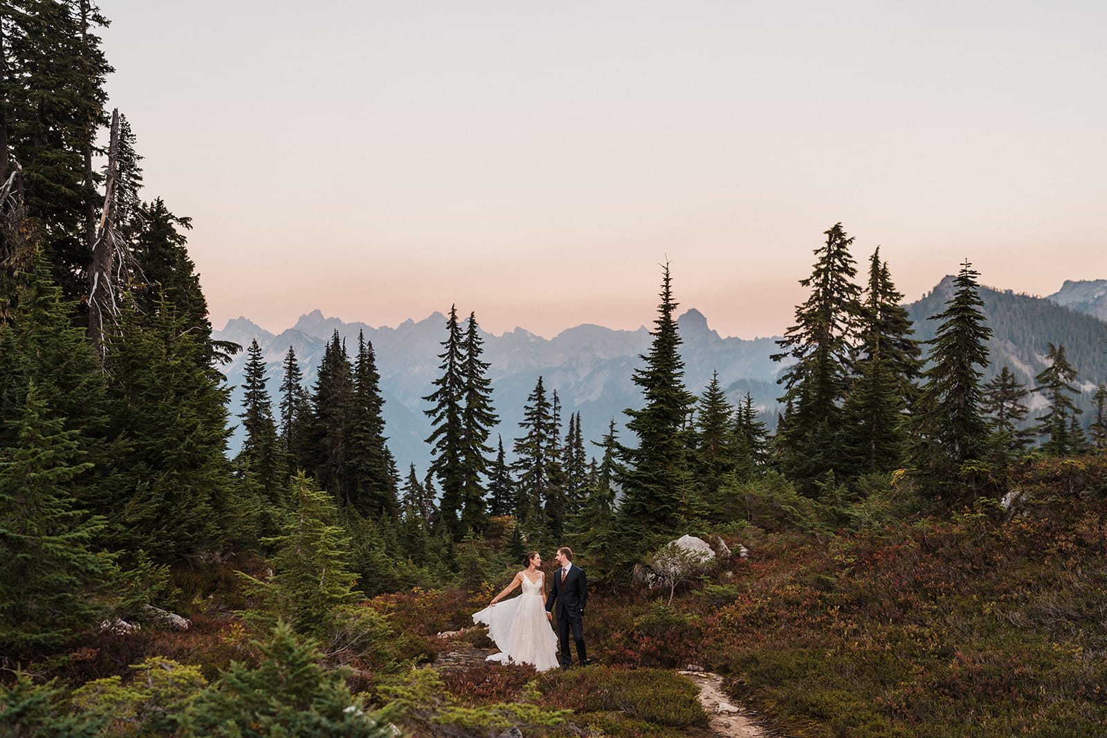 Bride and groom stand on a mountain trail at Snow Lake during their backpacking elopement. 
