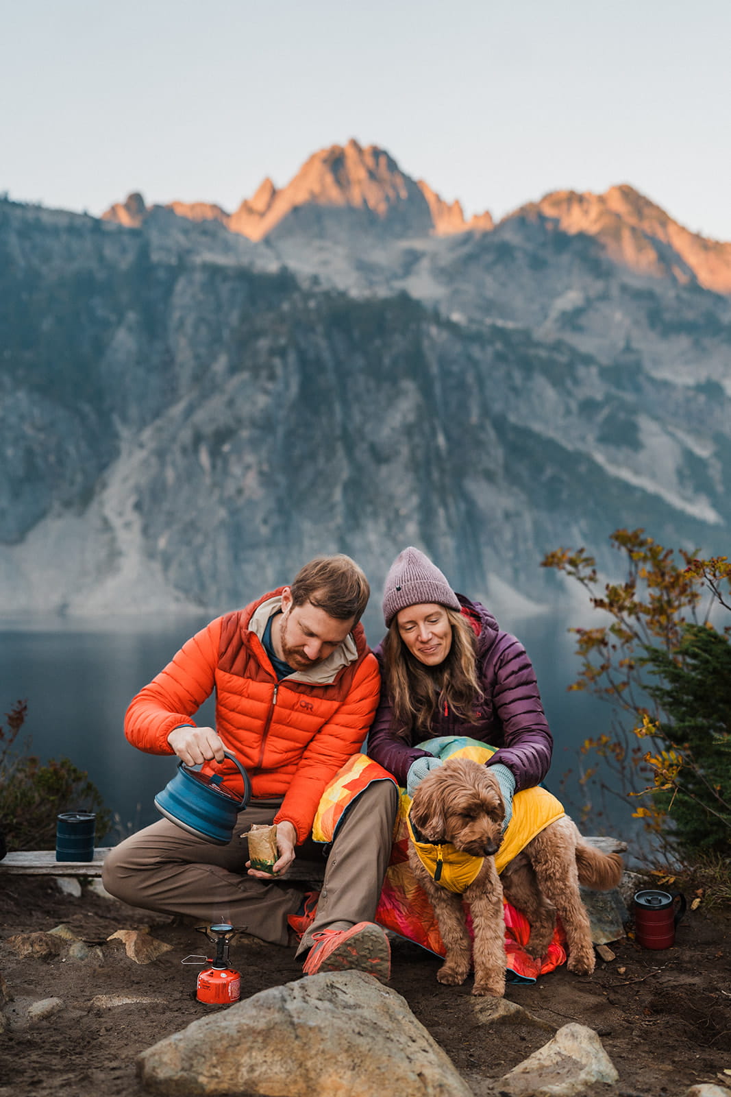 Couple sits on a log pouring coffee at sunrise during their backpacking elopement. 